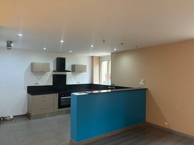 Cuisine vide avec un mur d'accent bleu, des armoires beiges, un comptoir noir et un éclairage encastré.