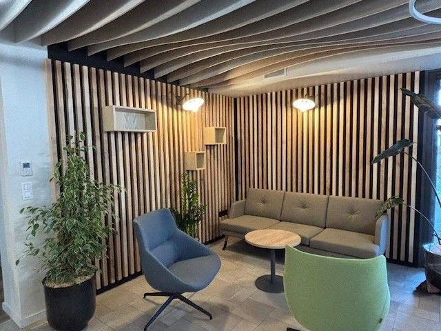 Salle d'attente moderne avec murs et plafond en lattes de bois, canapé gris, chaises et plantes en pot.