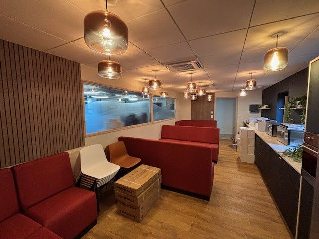 Une salle d'attente moderne avec des sièges rouges, des éléments en bois et des suspensions lumineuses en cuivre.