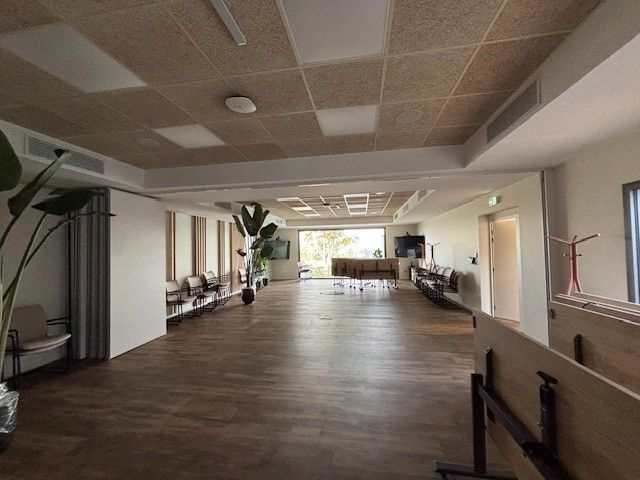 Salle d'attente spacieuse avec parquet, lambris au plafond et chaises le long du mur.