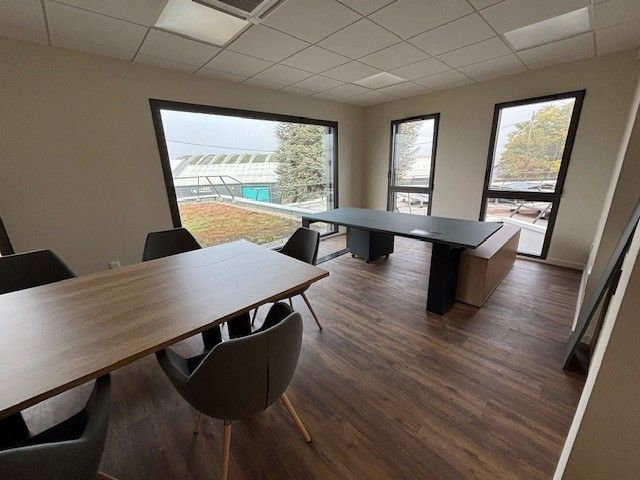 Salle de conférence avec deux tables, des chaises et de grandes fenêtres donnant sur la verdure.