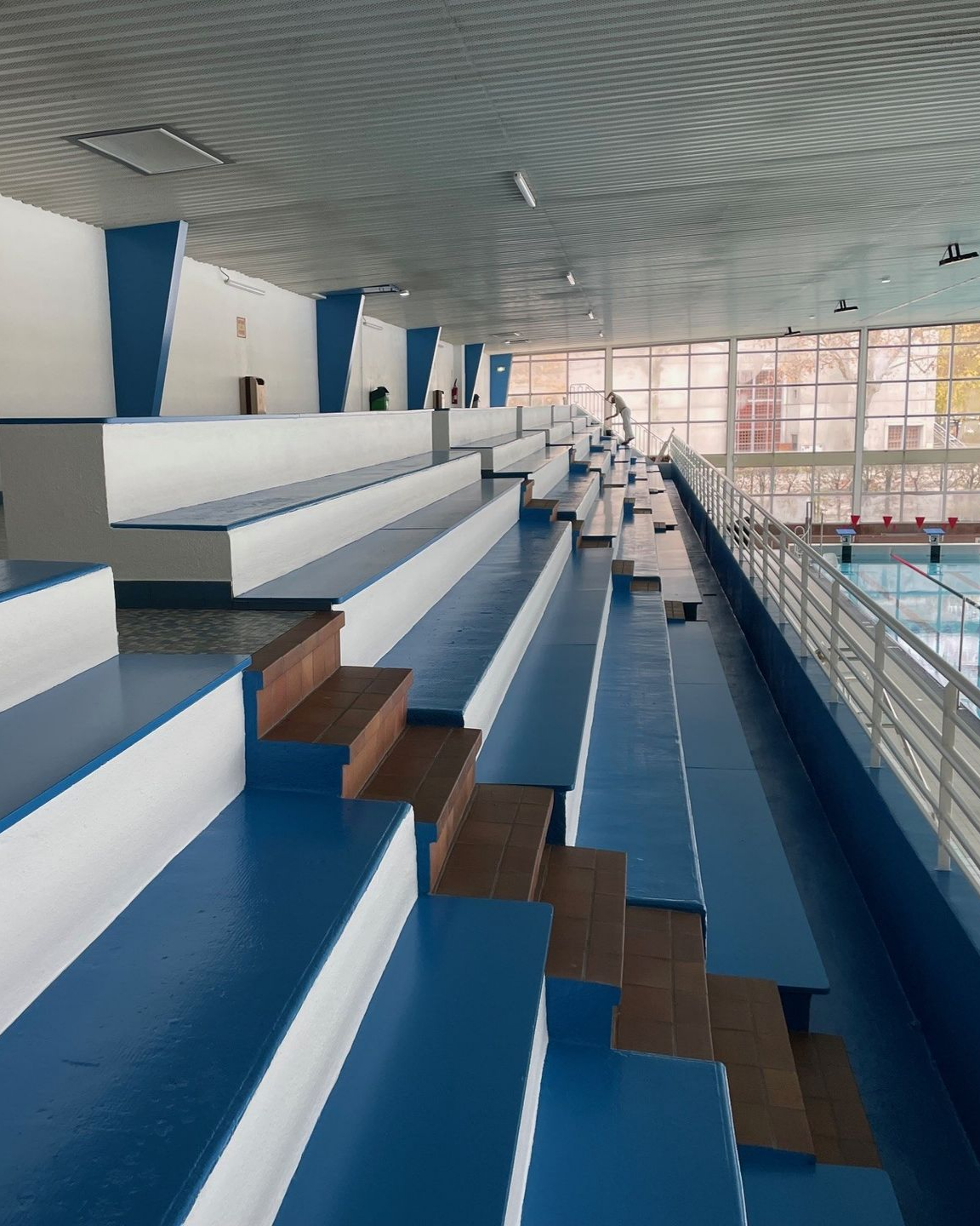 Piscine intérieure avec gradins bleus et blancs. Des marches en bois mènent aux rangées de gradins.