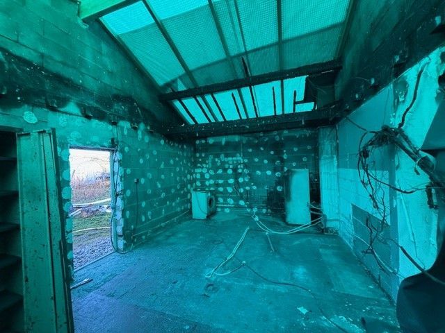 Intérieur d'une pièce en construction, murs et plafond apparents. Lumière teintée de vert, câblage visible.