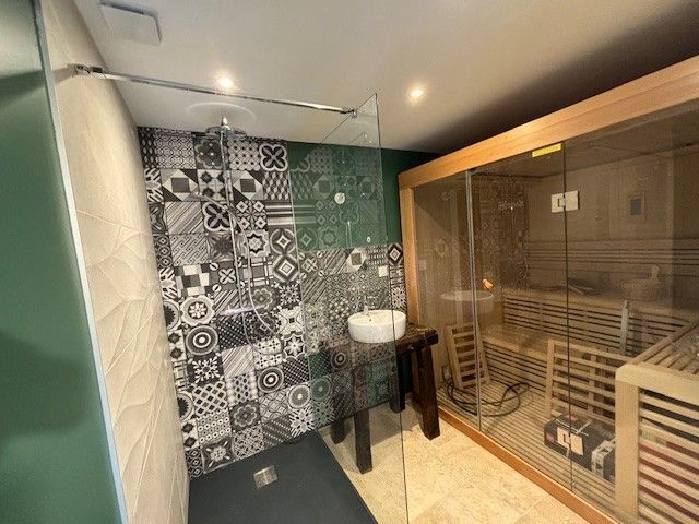 Espace douche avec mur carrelé à motifs, adjacent à un sauna en bois.