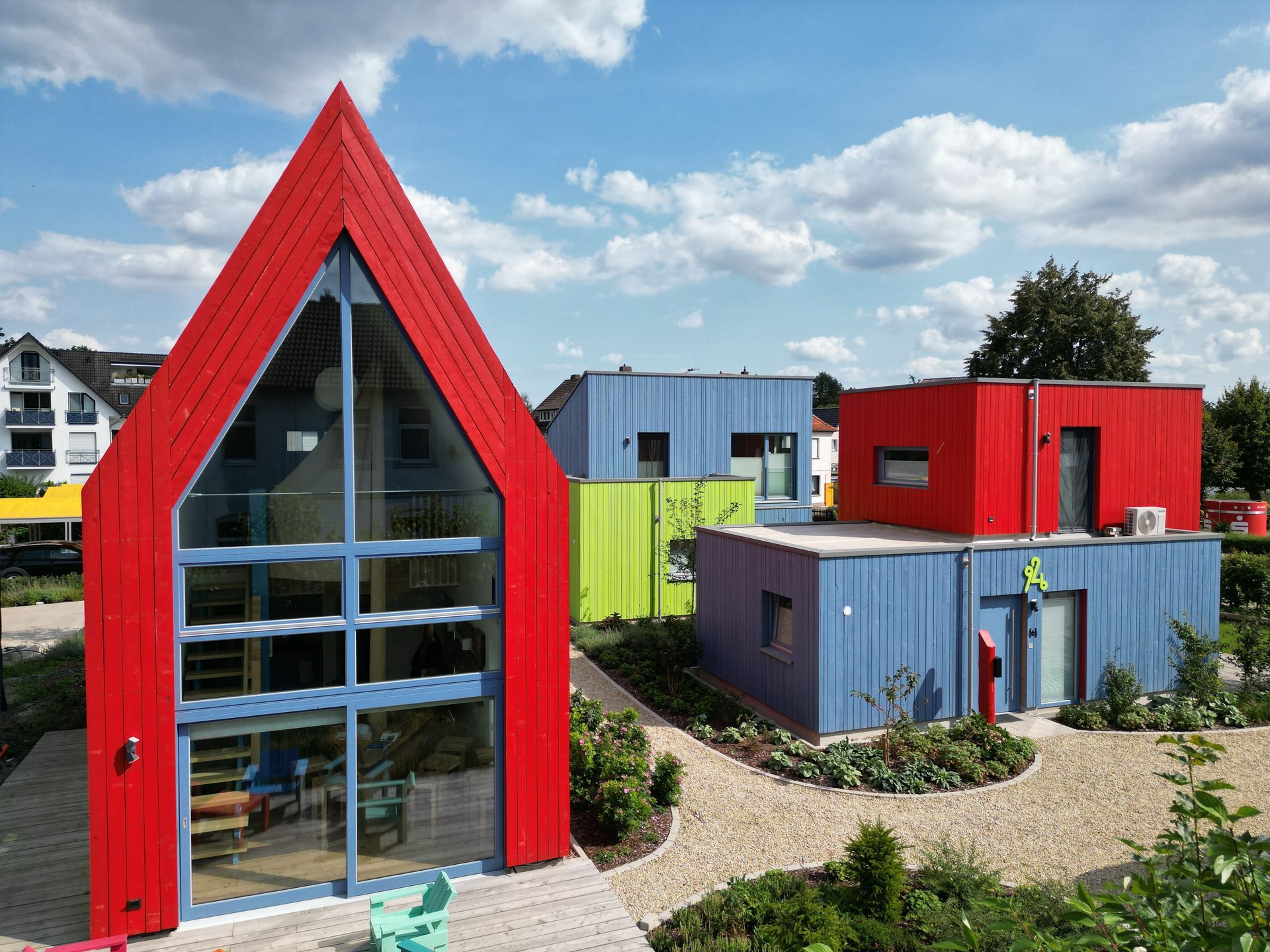 Rotes Spitzdachgebäude, dahinter Blau grüne Flachdachbauten