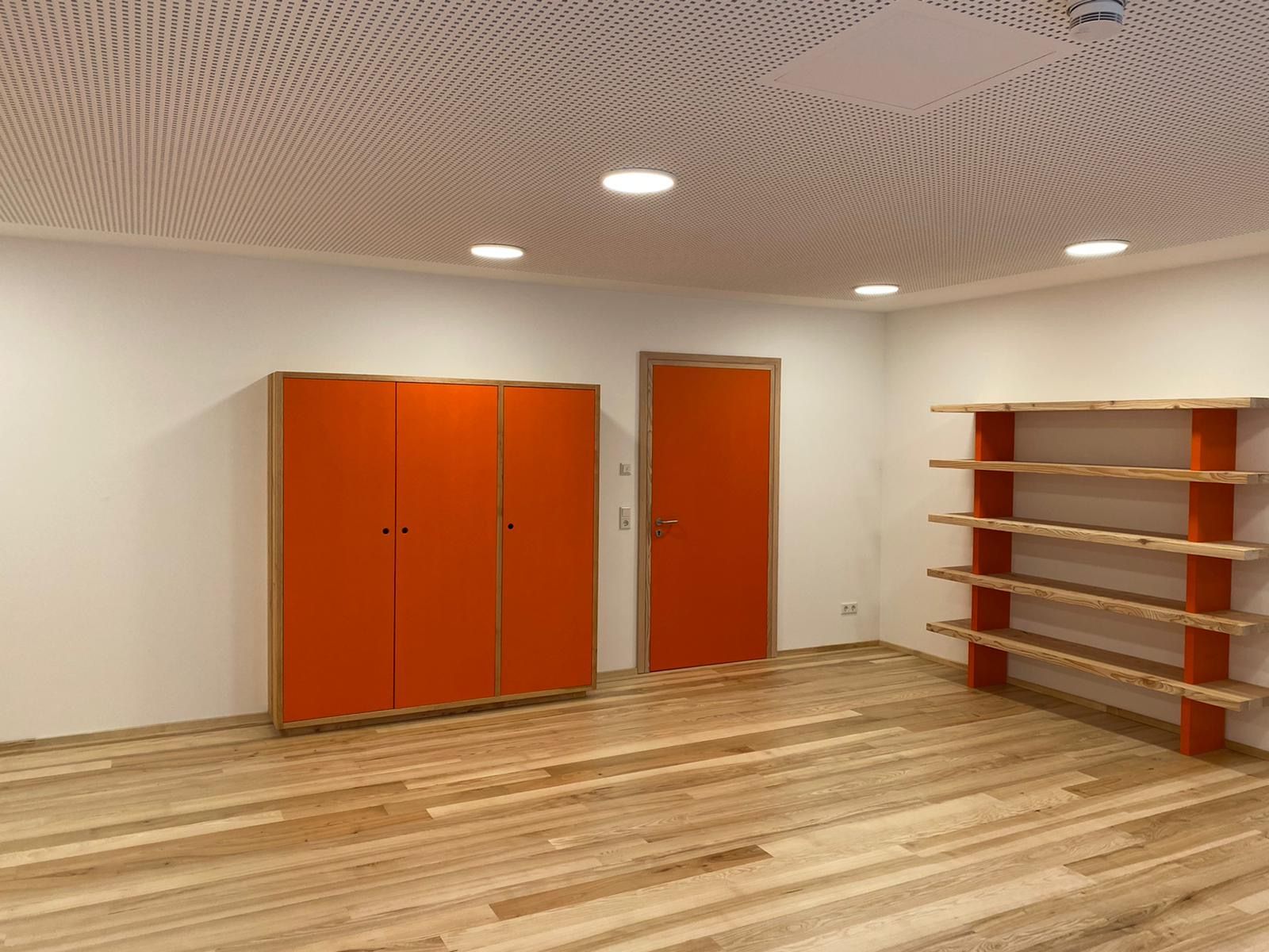 Holzboden auf dem ein orangener Schrank steht neben einer Tür