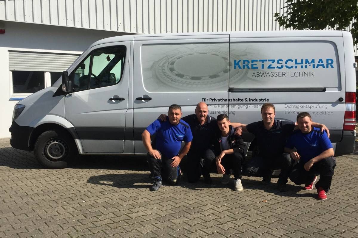 Fünf Personen in blauen Hemden posieren vor einem Firmenwagen mit der Aufschrift „KRETZSCHMAR“.