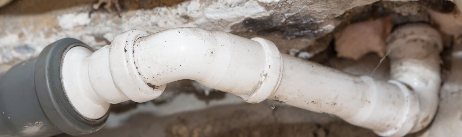 Weiße Kunststoff-Wasserleitungen mit dunklen Ablagerungen, eingelassen in einer rissigen Wand.