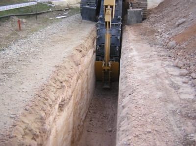 Una excavadora cavando una zanja larga en la tierra en un sitio de construcción.