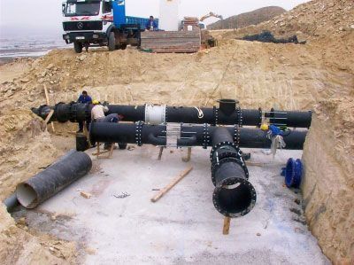 Sitio de construcción con trabajadores ensamblando grandes tuberías de aguas negras en un área excavada.