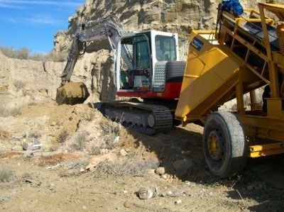Excavadora cavando tierra y depositándola en un remolque amarillo en un paisaje desértico.