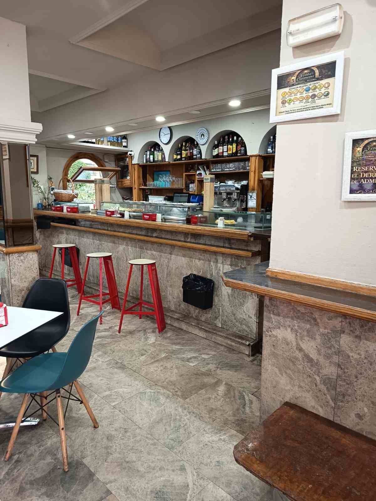Interior de un bar restaurante con taburetes rojos, barra de madera y mesas en un acogedor comedor