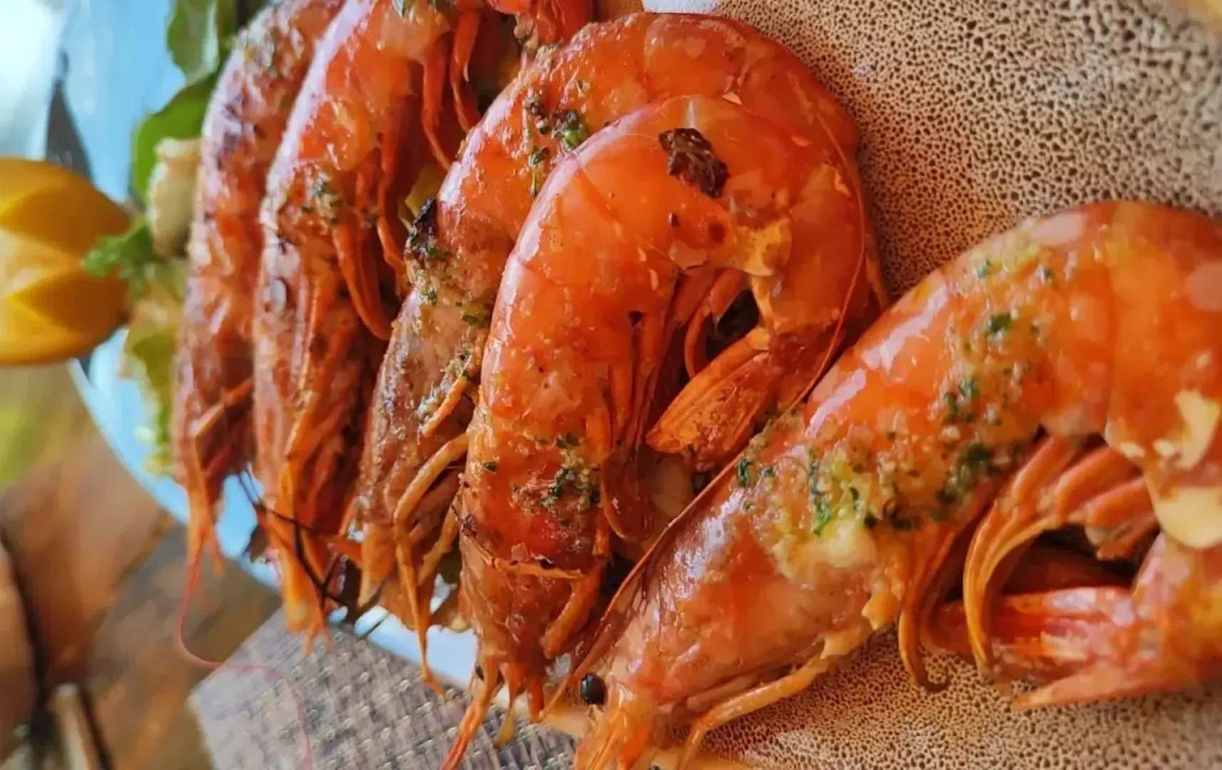 Una hilera de gambas cocidas y sazonadas, dispuestas en una fuente, adornadas con hierbas y servidas con rodajas de limón.