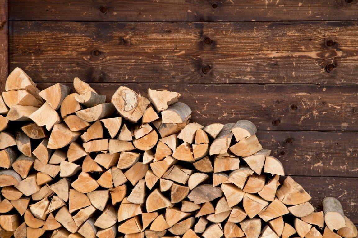 Leña partida apilada contra una pared de madera desgastada.