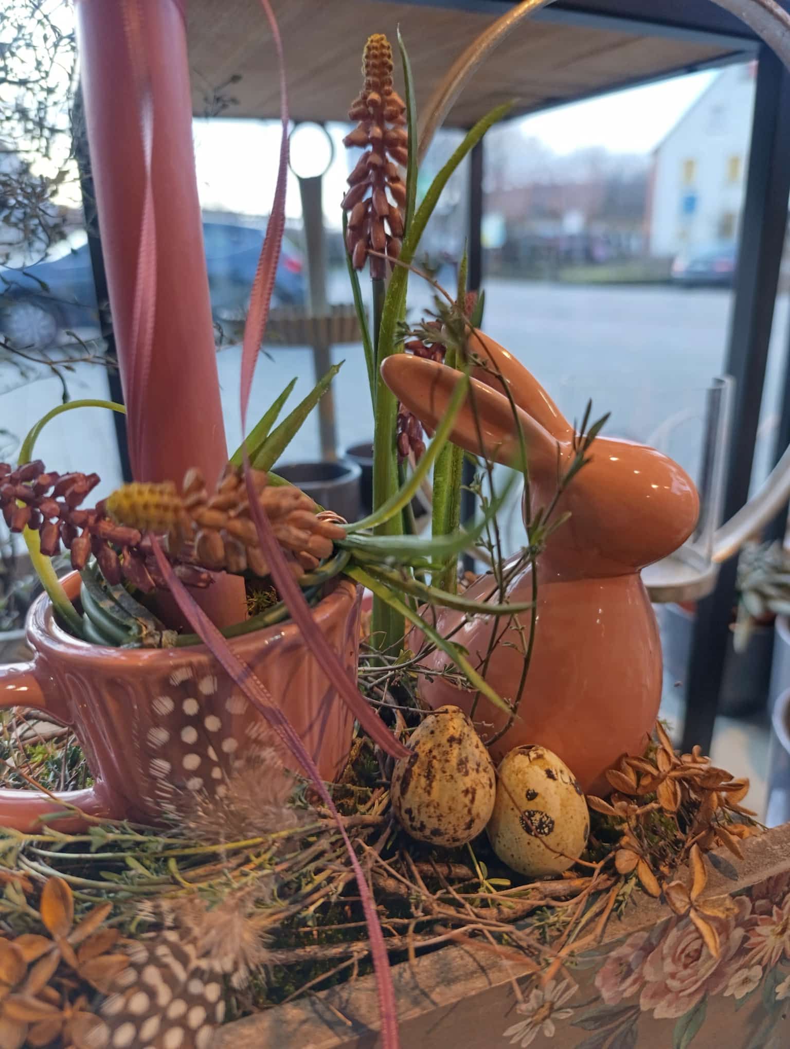 Ein Keramikhase sitzt auf einem Tisch mit Blumen und Eiern.