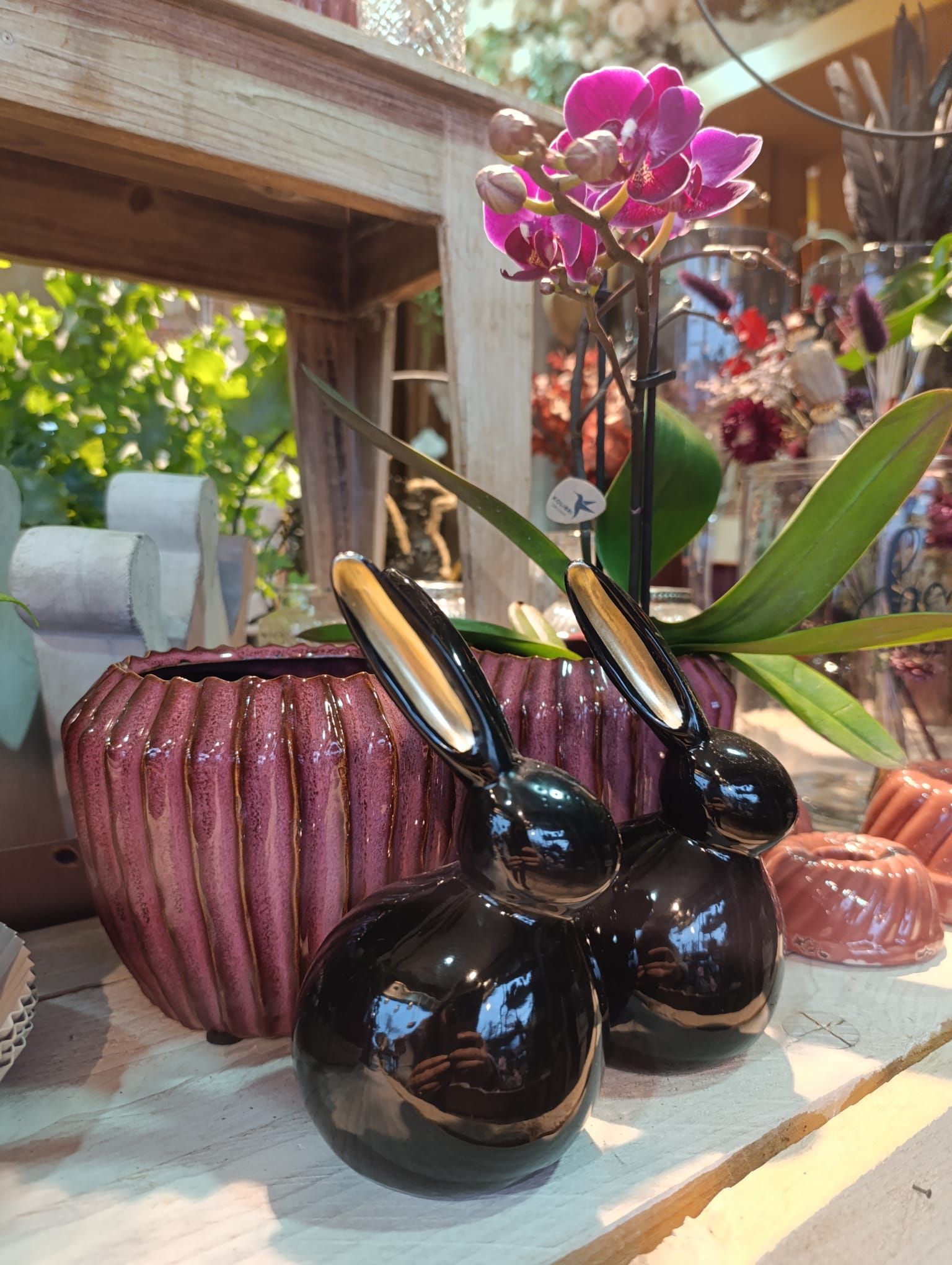 Zwei schwarze Keramikhasen sitzen neben einer rosa Vase mit einer lila Blume darin.