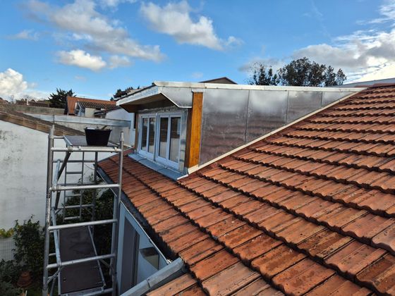 Toit avec des tuiles rouges, des échafaudages et un bâtiment blanc.