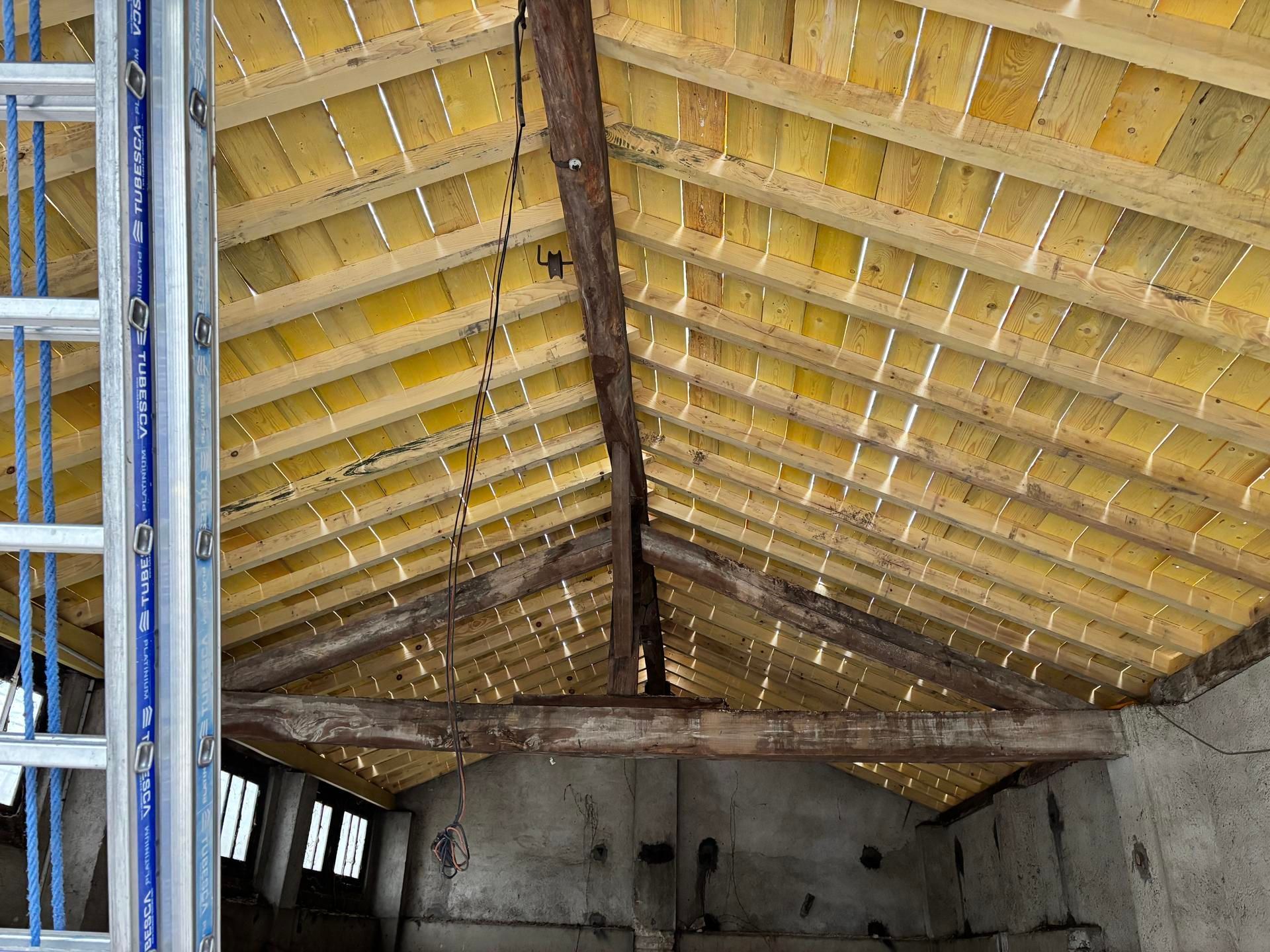 Intérieur d'un bâtiment en construction avec charpente apparente en bois et murs en béton brut.