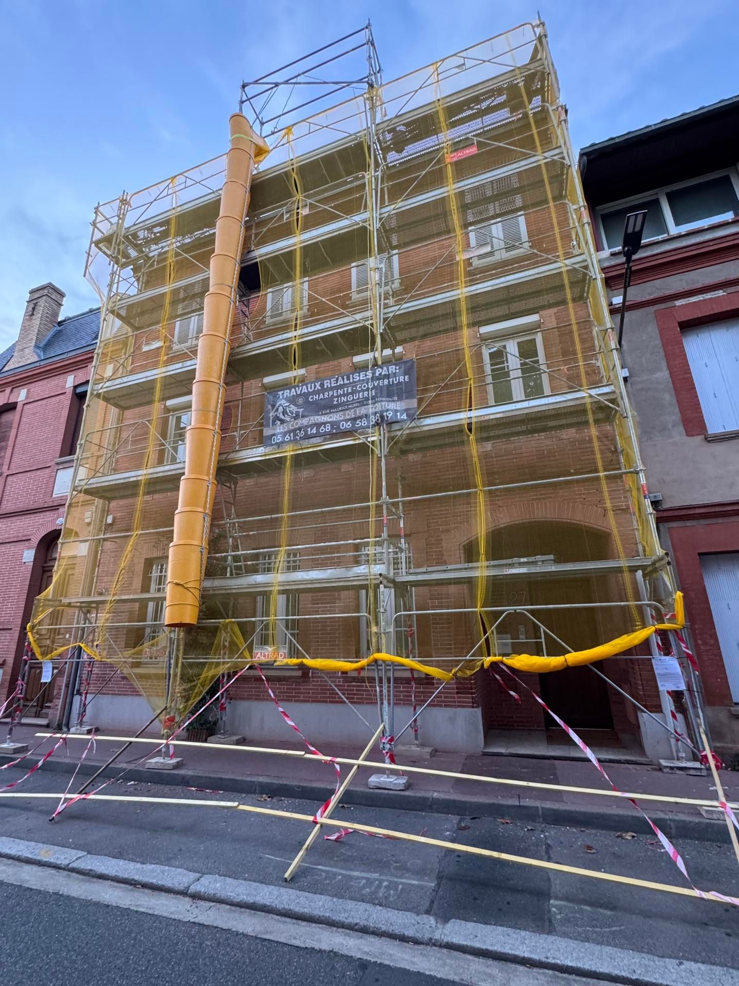 Des échafaudages recouvrent un bâtiment en briques lors de travaux de rénovation extérieure dans une rue.