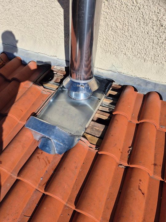 Solin de cheminée sur tuiles en terre cuite avec conduit de ventilation métallique et ruban d'étanchéité bleu.