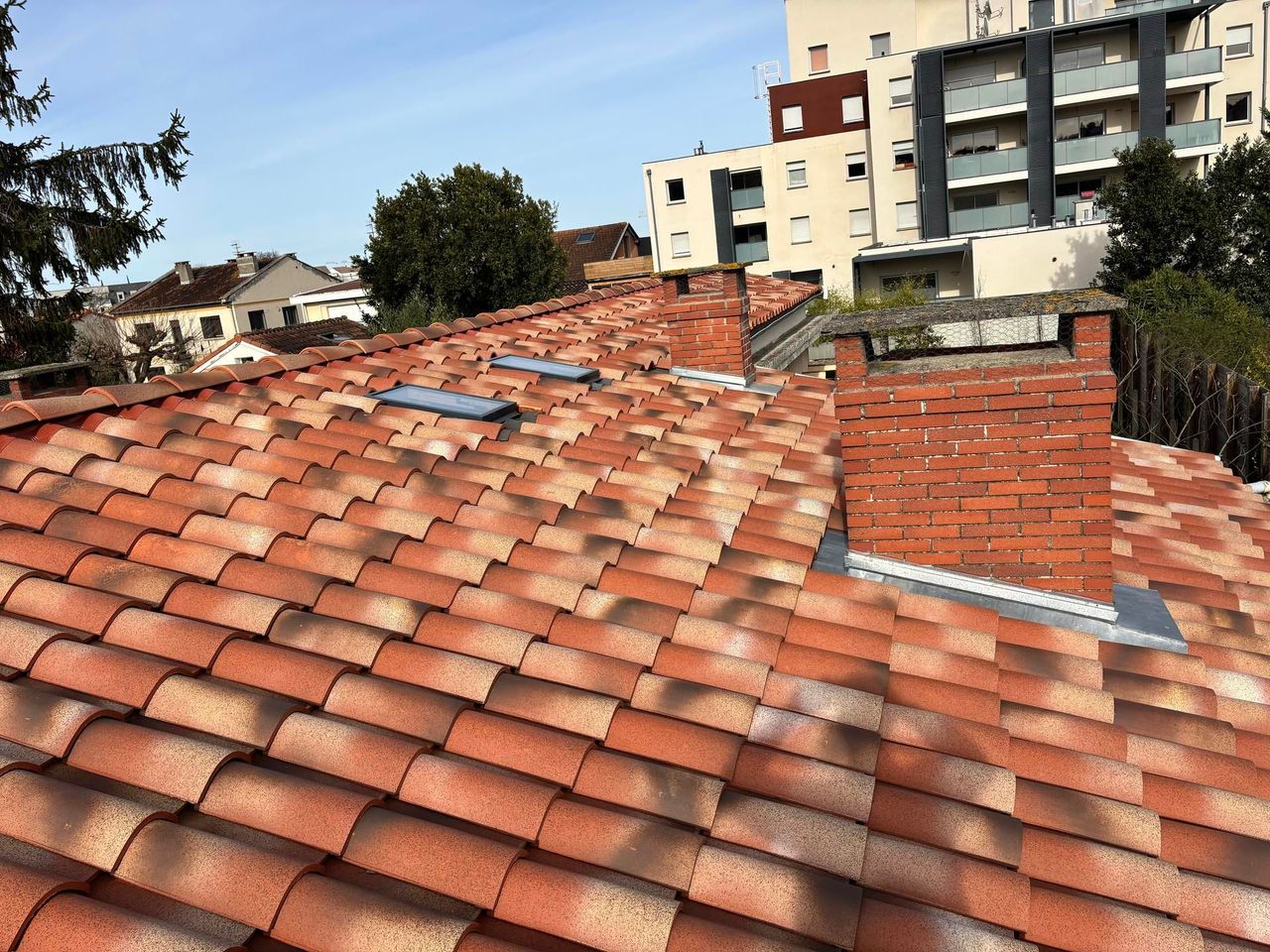 Toits de tuiles en terre cuite rouge et aérations dans un quartier résidentiel sous un ciel bleu