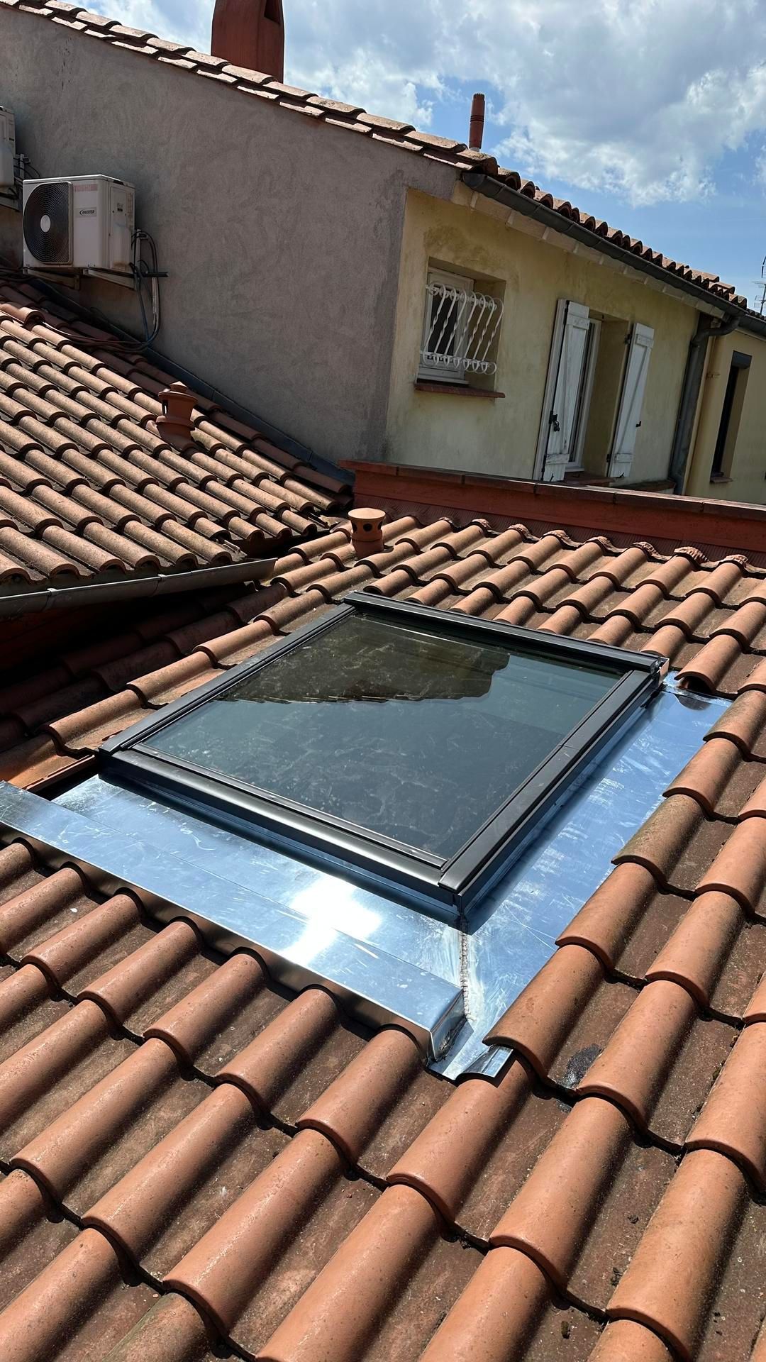 Fenêtre de toit sur un toit de tuiles en terre cuite rouge à côté d'une maison en stuc.