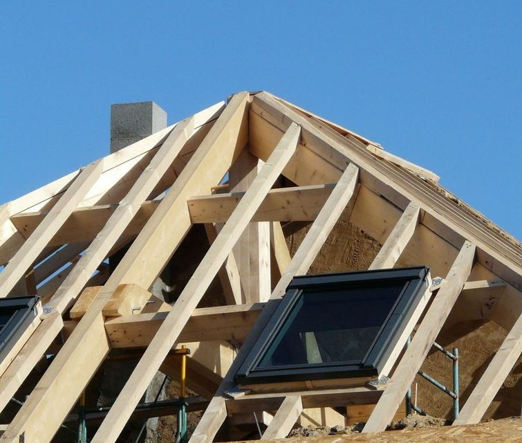 Charpente de toit en bois en construction avec une fenêtre de toit noire.