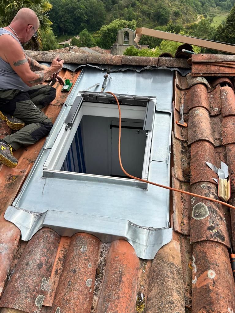 Un ouvrier installe un puits de lumière sur un toit en tuiles, avec une grande ouverture de toit et des outils à proximité.