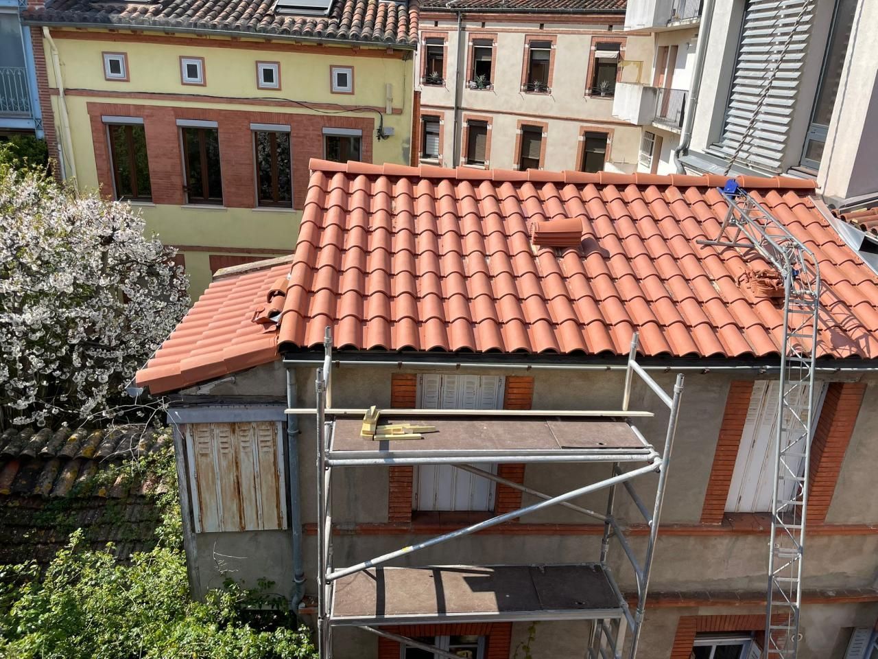 Petit bâtiment en cours de rénovation avec une toiture en tuiles, avec des échafaudages, vue d'en haut depuis une cour.