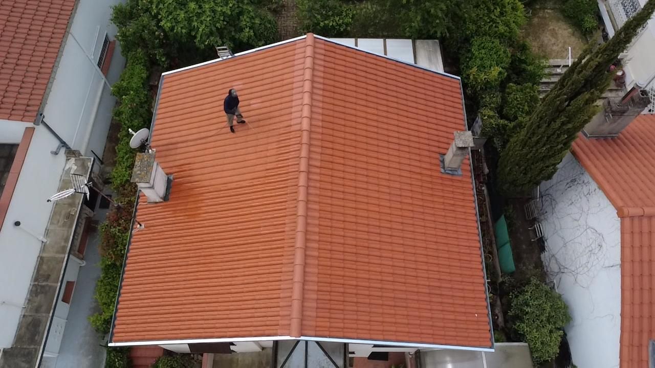 Vue aérienne d'un toit de tuiles rouges avec une personne debout près du sommet, entourée d'arbres.