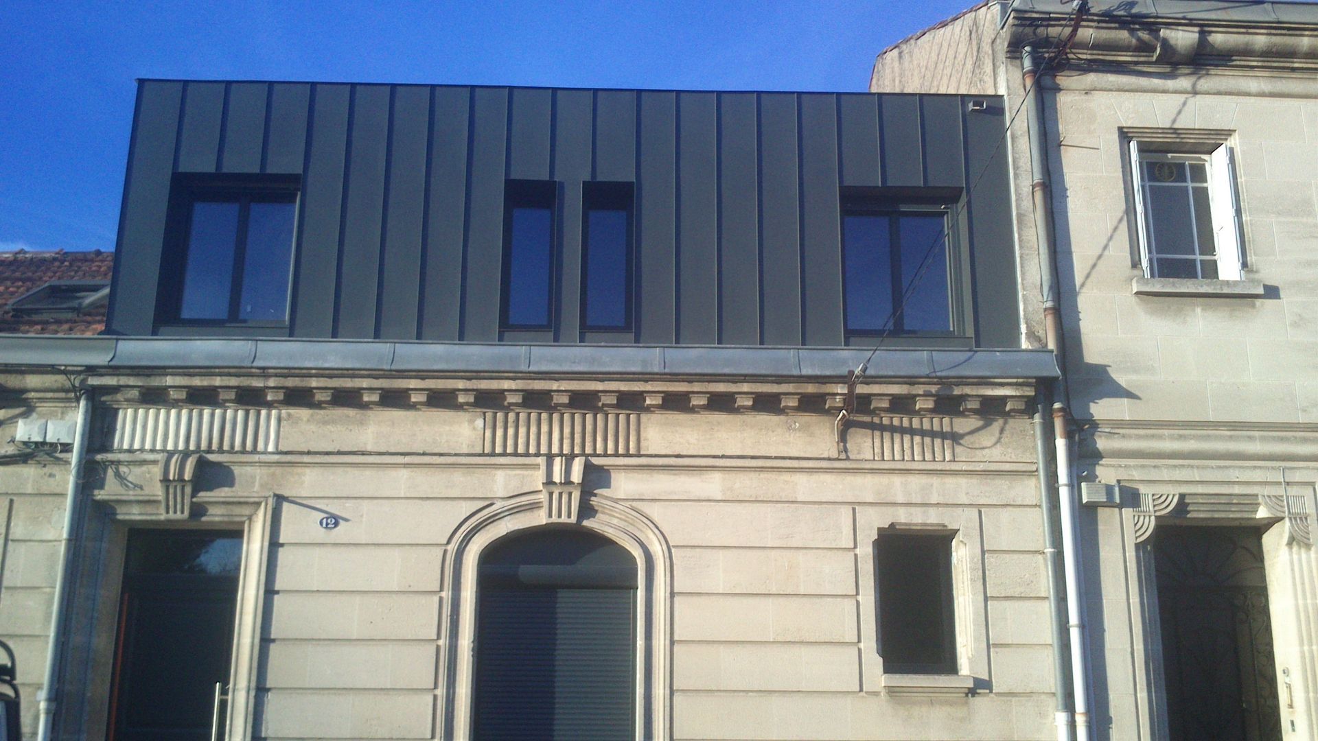 Une maison avec une surélévation avec des planches grises