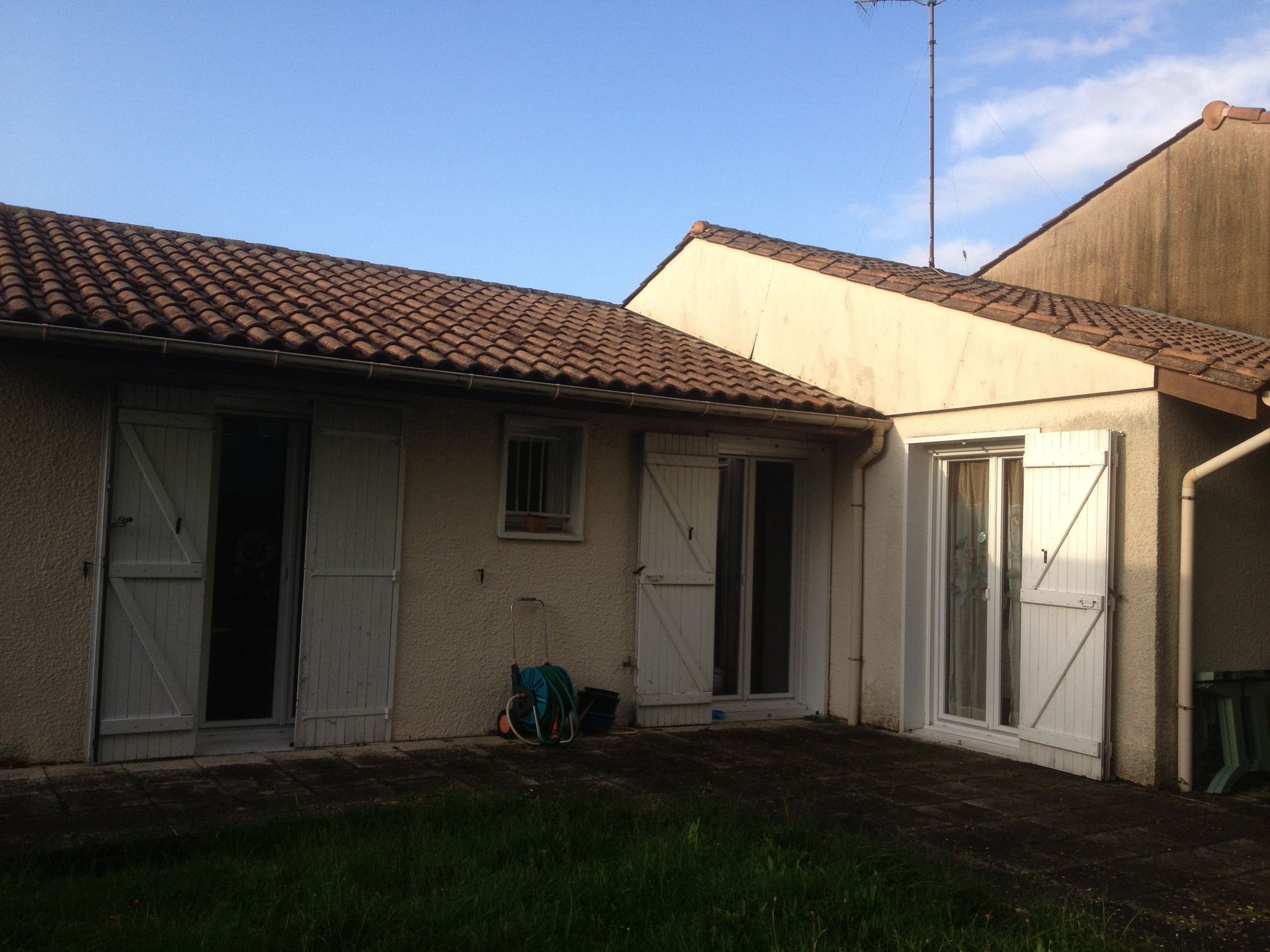 Une maison aux murs jaunes et aux volets blancs avant une surélévation