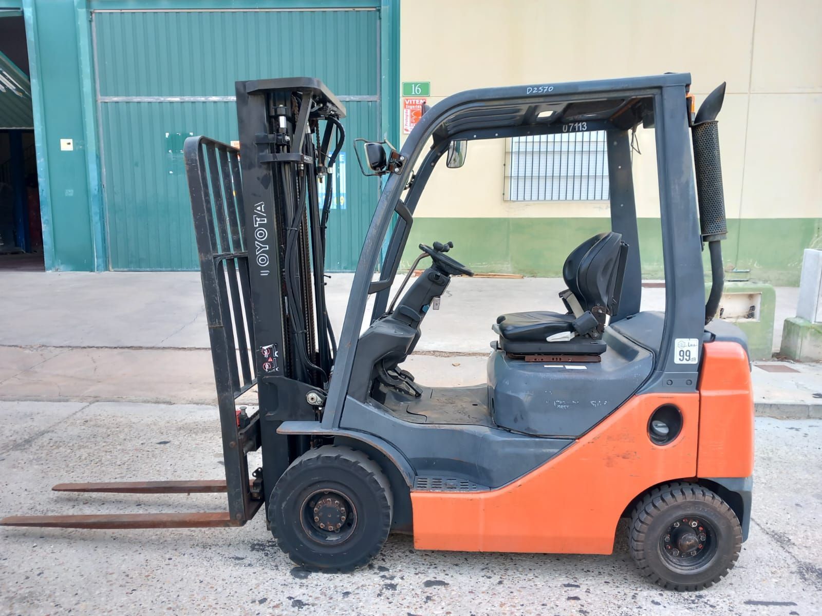 Una carretilla elevadora de color naranja y negro está estacionada frente a un edificio.