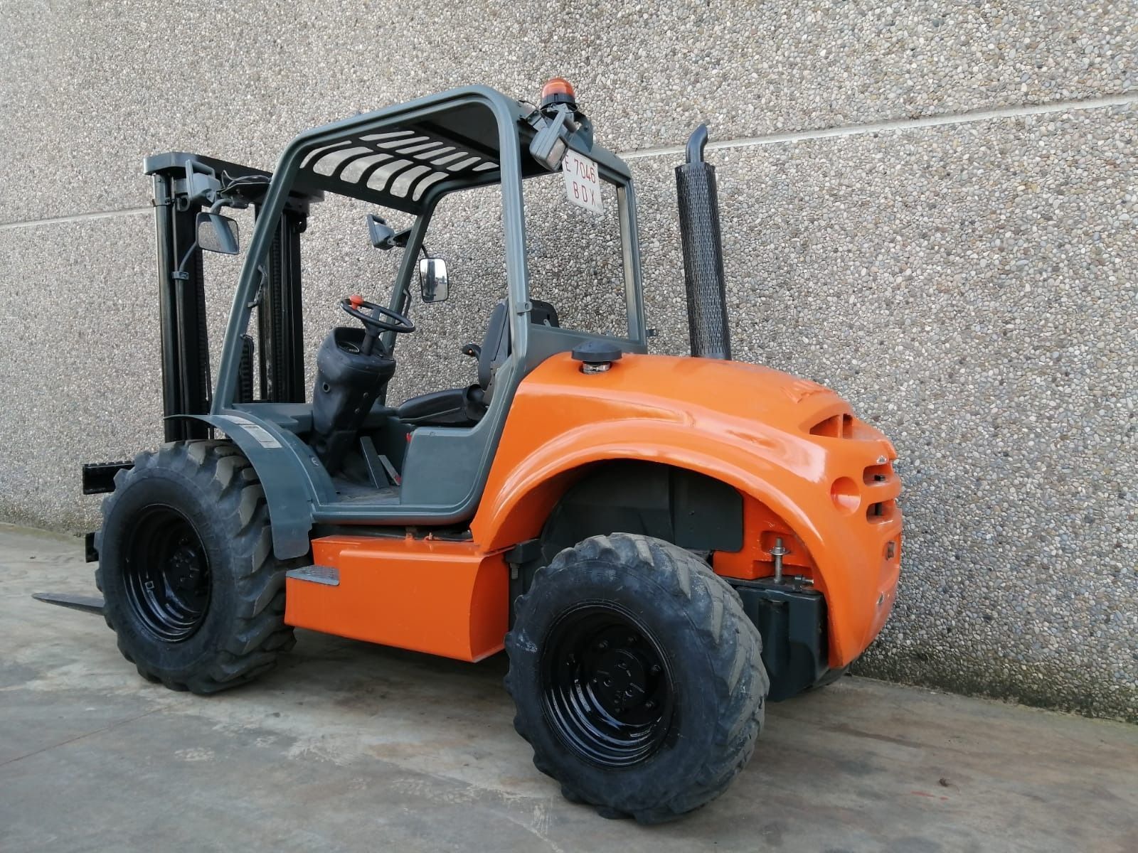 Una carretilla elevadora naranja está estacionada frente a un muro de hormigón.