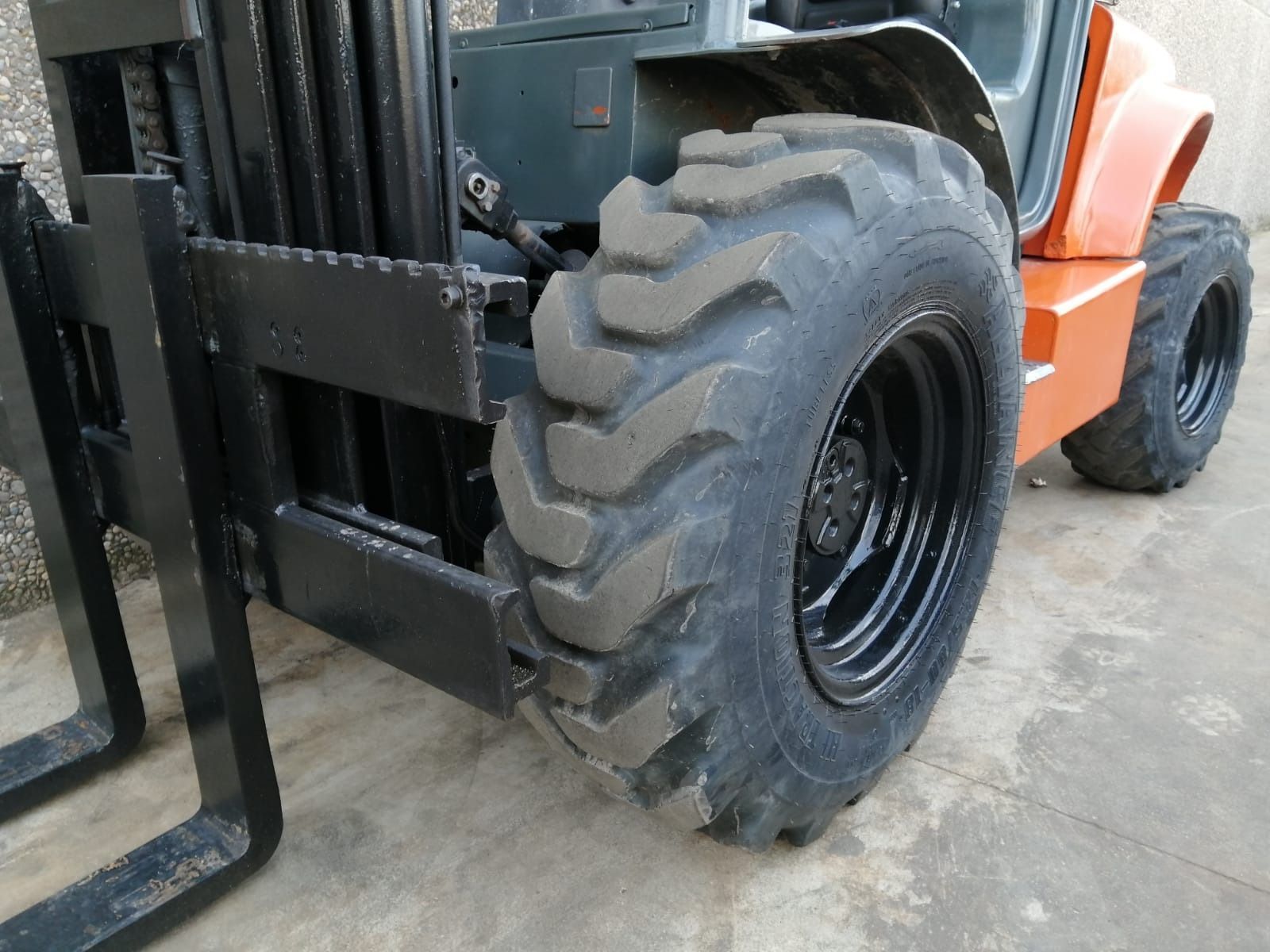 Una carretilla elevadora con un neumático grande está estacionada sobre una superficie de concreto.