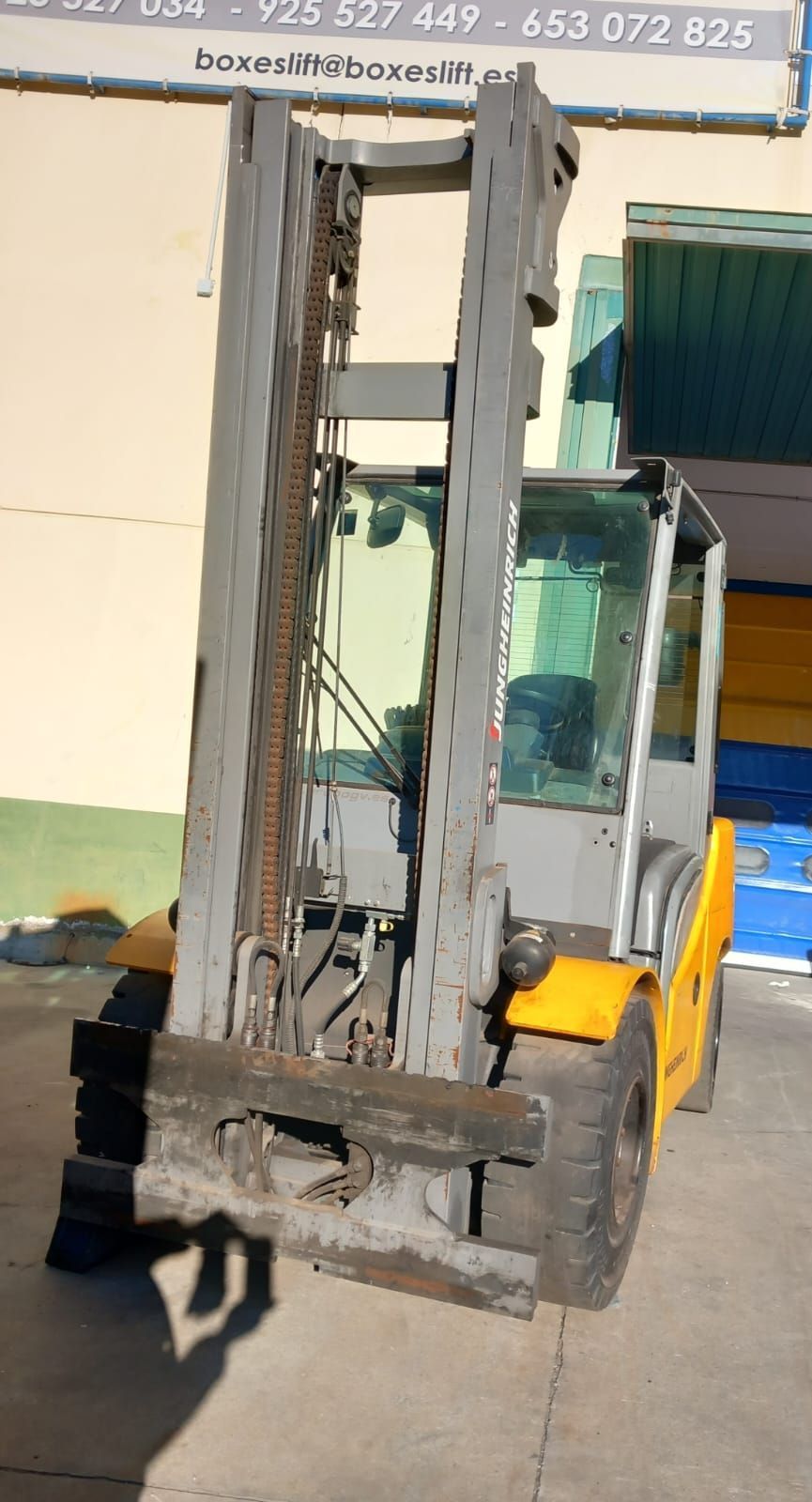 Una carretilla elevadora amarilla y gris está estacionada frente a un edificio.