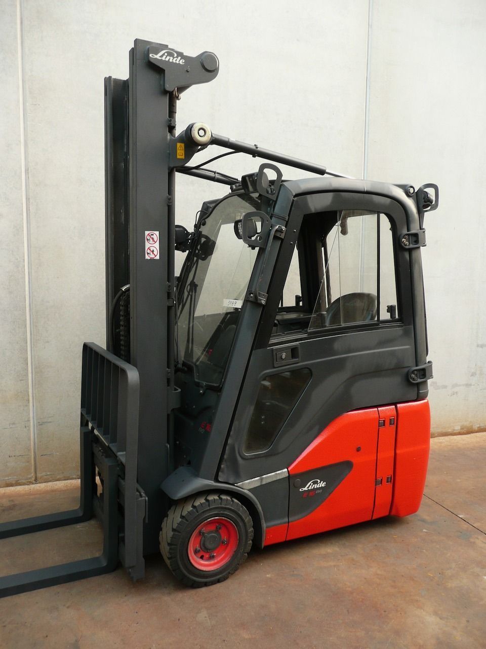 Una carretilla elevadora roja y negra está estacionada frente a un muro de hormigón.