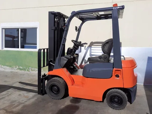 Una carretilla elevadora naranja y azul está estacionada frente a un edificio.