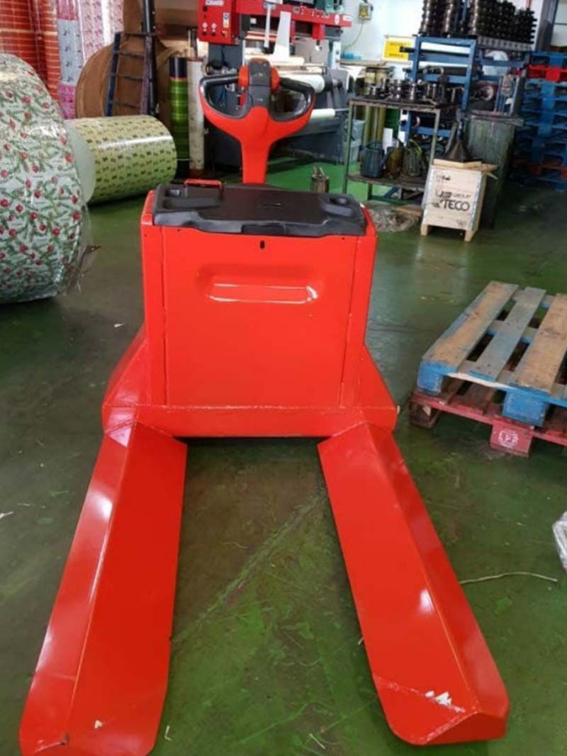 Una carretilla elevadora roja está sobre un suelo verde en un almacén.