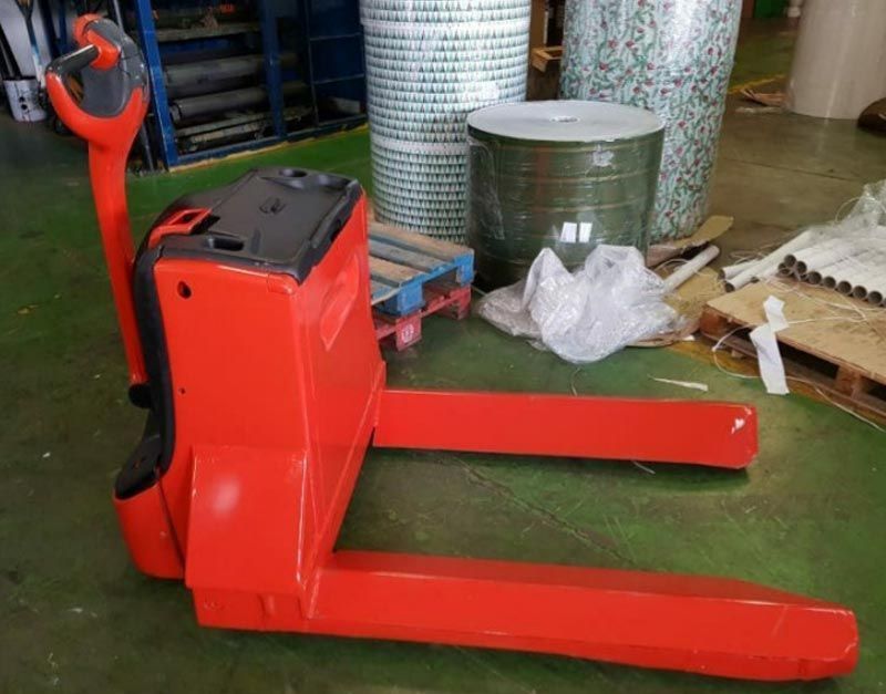 Una transpaleta roja está parada en el suelo en un almacén.