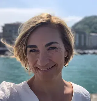 Una mujer sonríe a la cámara frente a un cuerpo de agua.