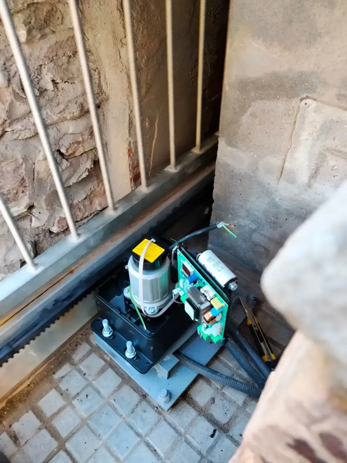 Mecanismo de apertura de puerta motorizado con motor eléctrico, placa de circuito y estructura metálica.