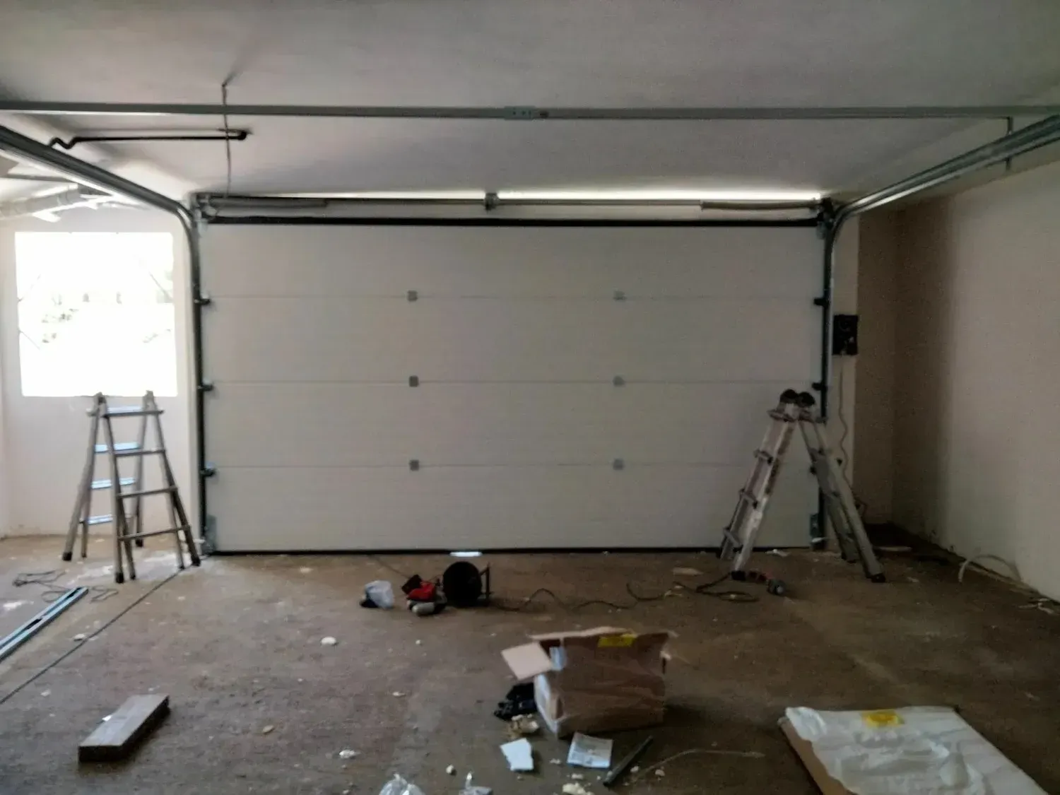 Interior del garaje con puerta blanca nueva. Hay escaleras y herramientas.