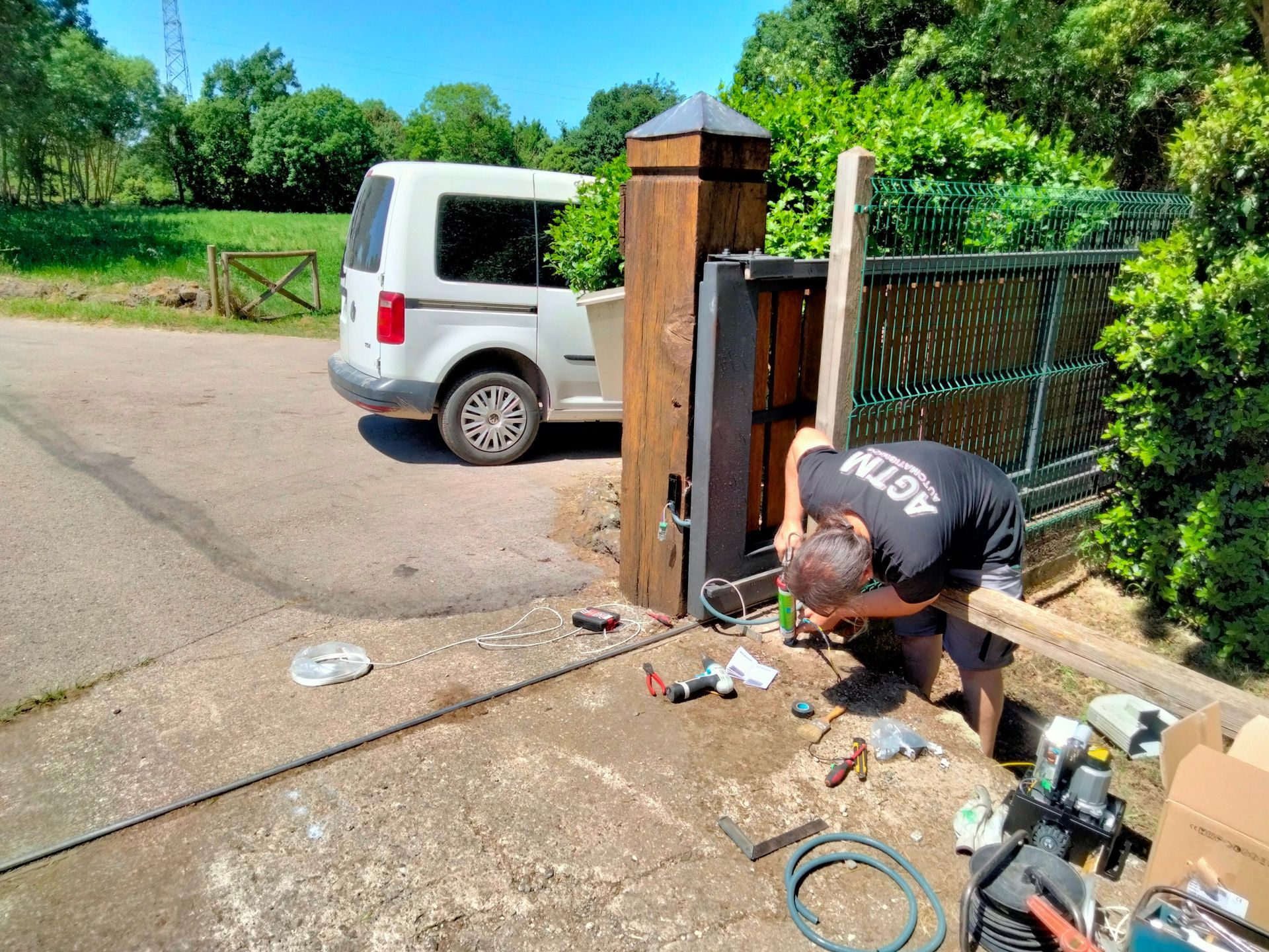 Una persona trabaja en una puerta automática, con una furgoneta aparcada cerca. Afuera, un día soleado.