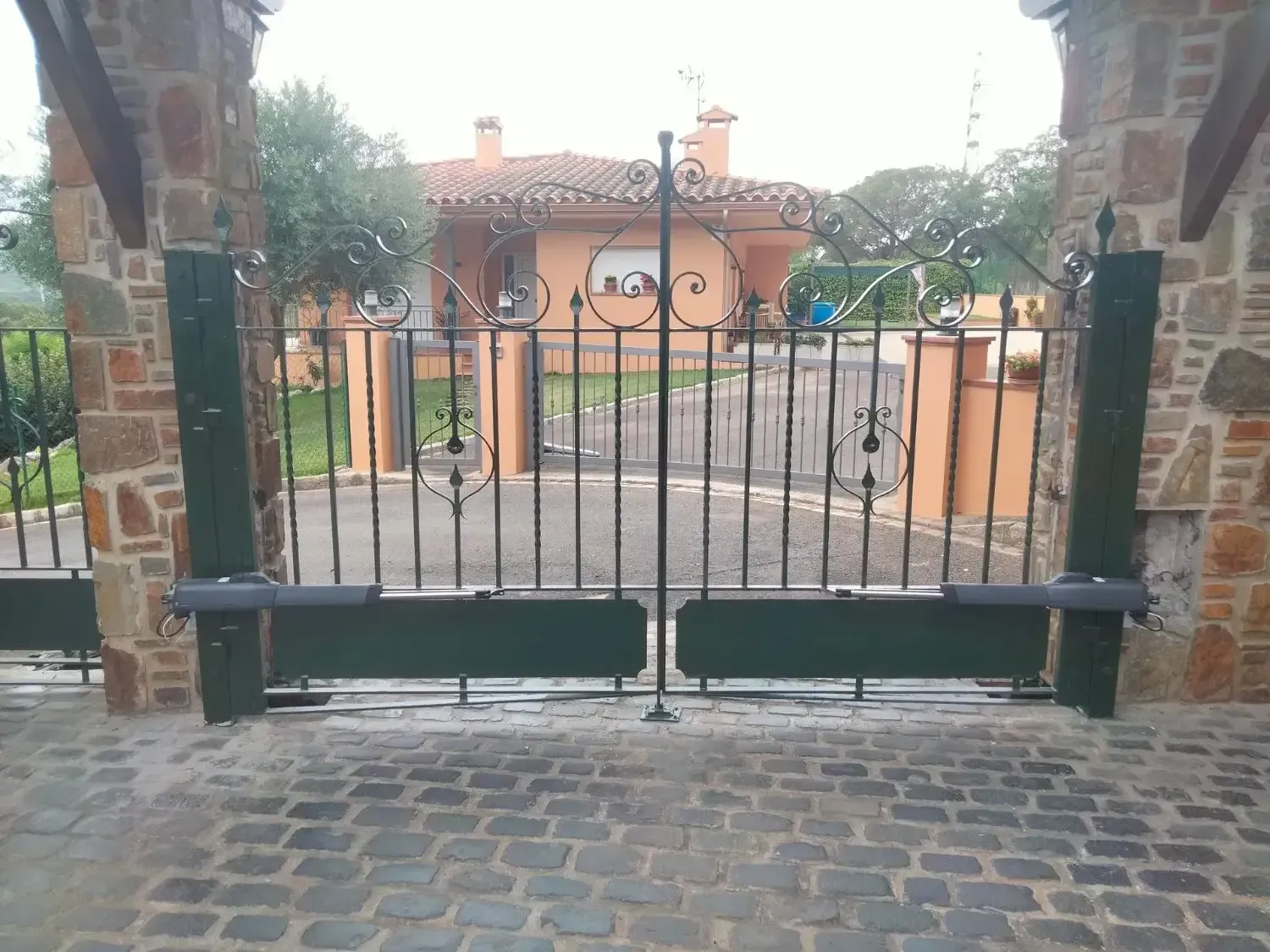 Puerta de hierro forjado negro frente a una casa. Columnas de ladrillo a ambos lados.