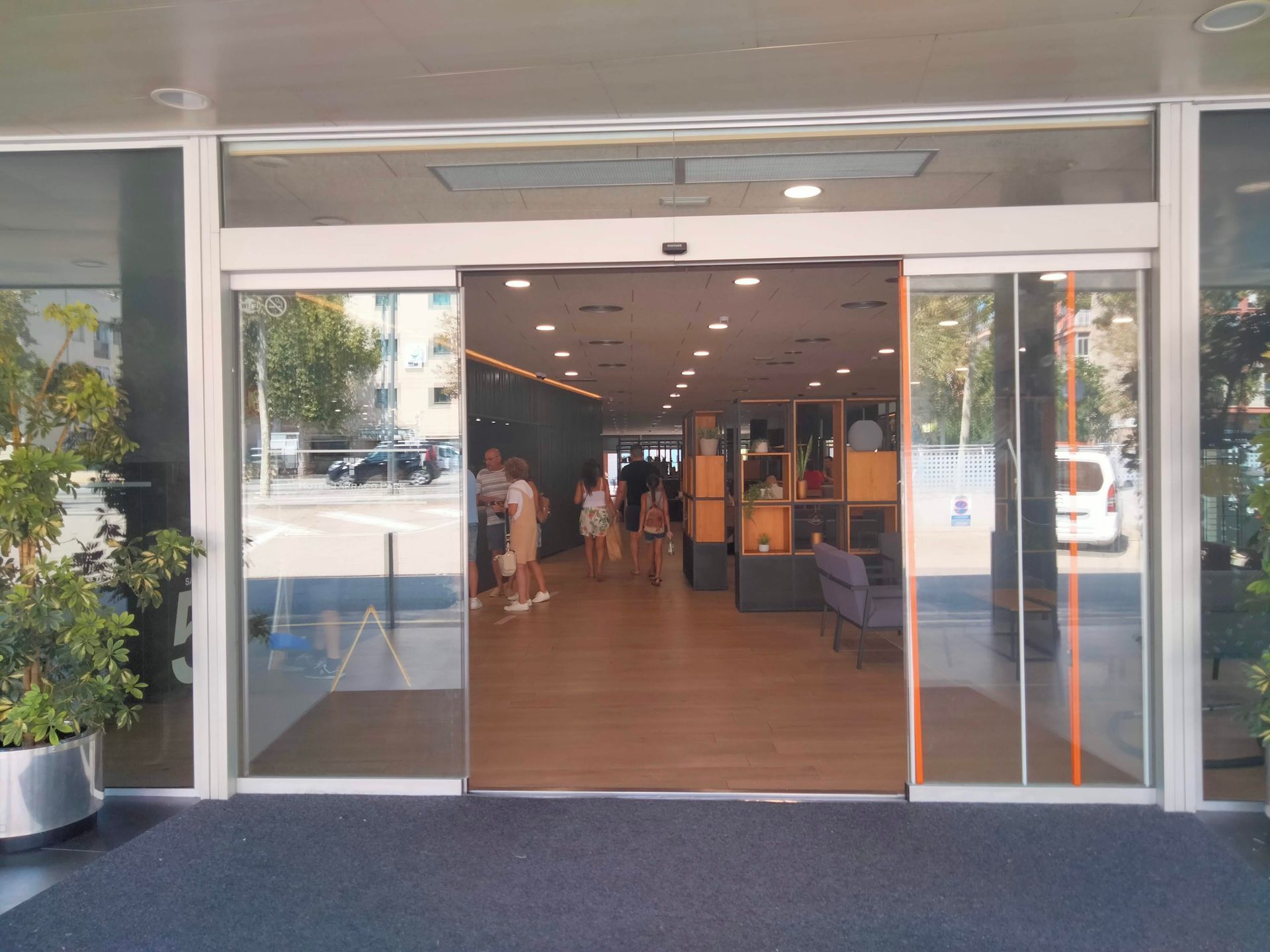 Las puertas automáticas de vidrio se abren a un vestíbulo bien iluminado con gente caminando hacia el interior.