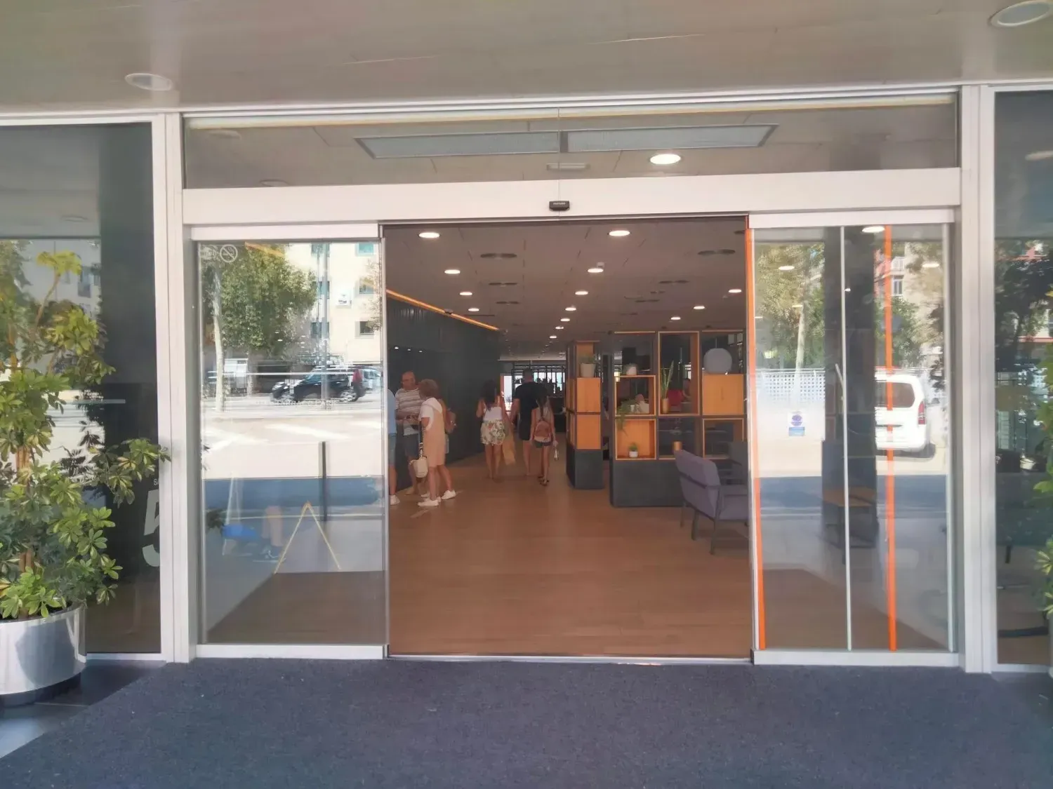 Las puertas automáticas de vidrio se abren a un vestíbulo bien iluminado con gente caminando hacia el interior.