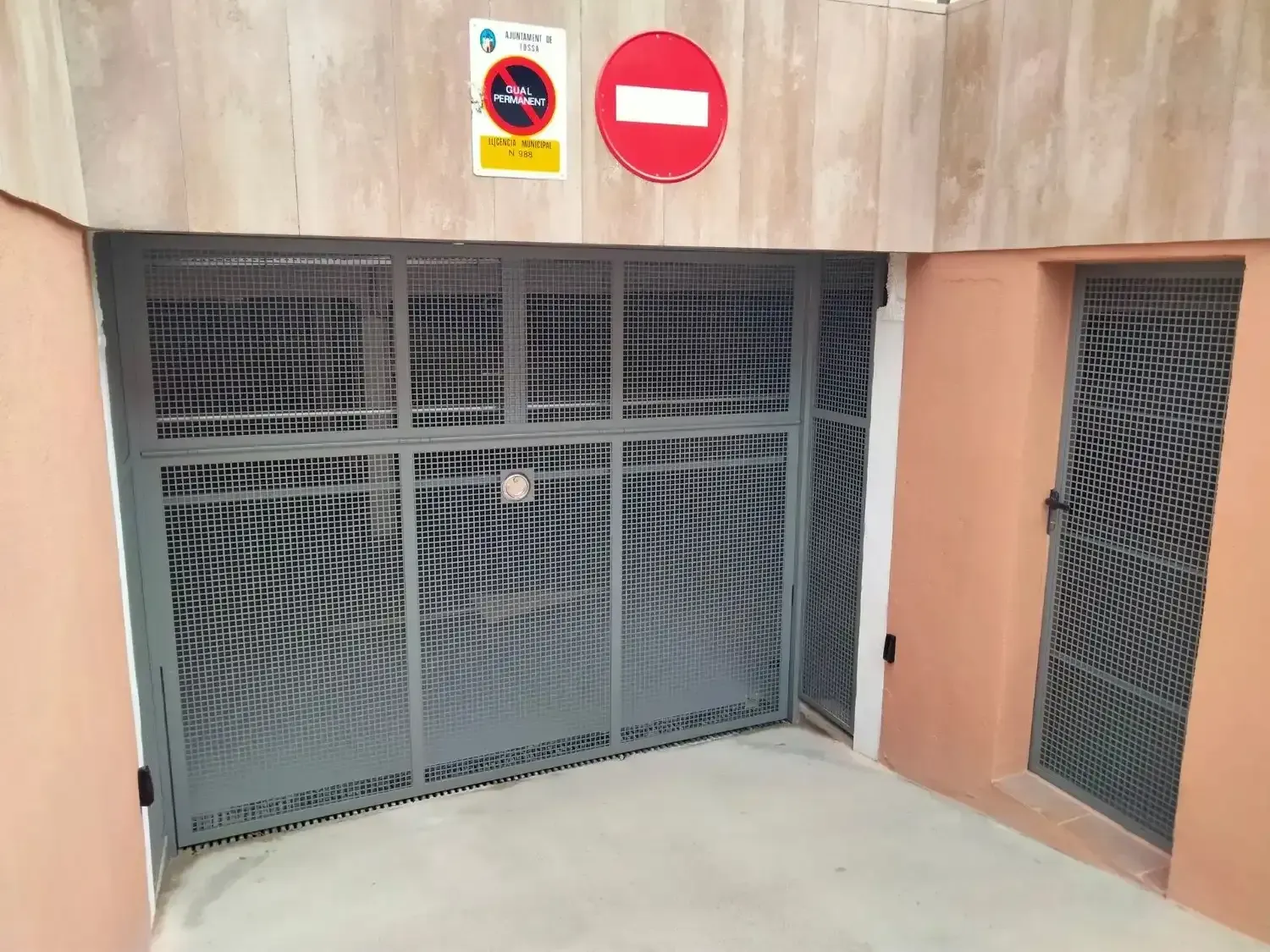 Entrada a un estacionamiento con puerta metálica y cartel de 