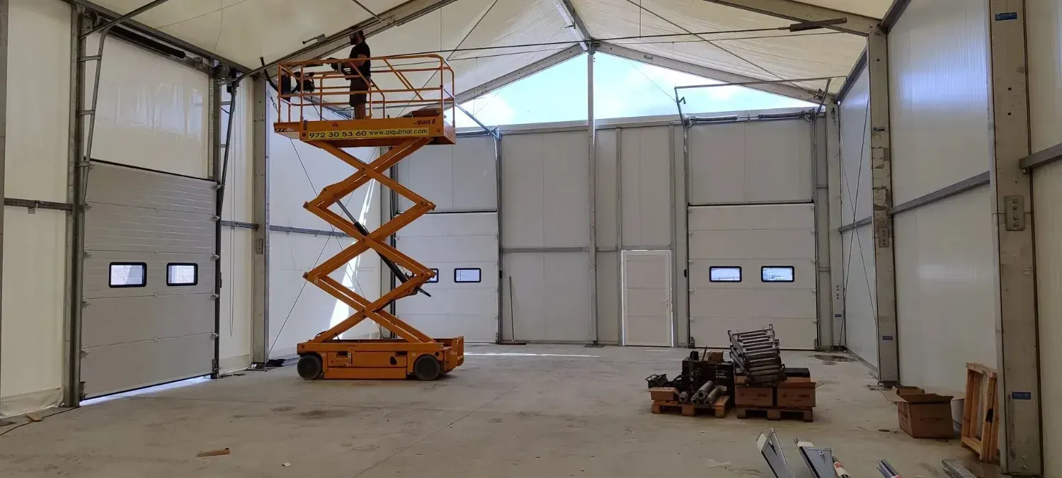 Hombre en un elevador de tijera dentro de un gran edificio industrial.