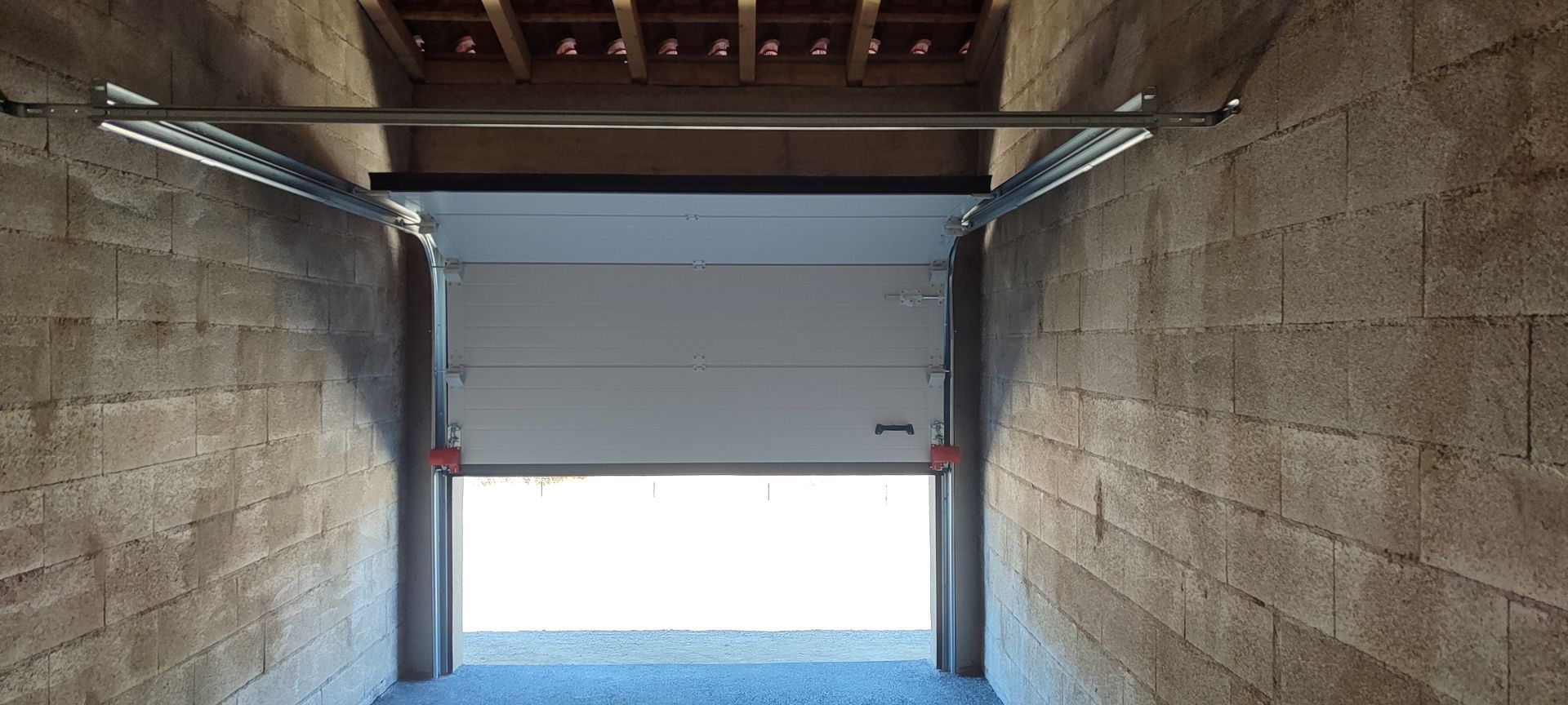 Puerta de garaje parcialmente abierta con paredes de bloques de hormigón a ambos lados. Se ven barras de metal y un techo de madera.